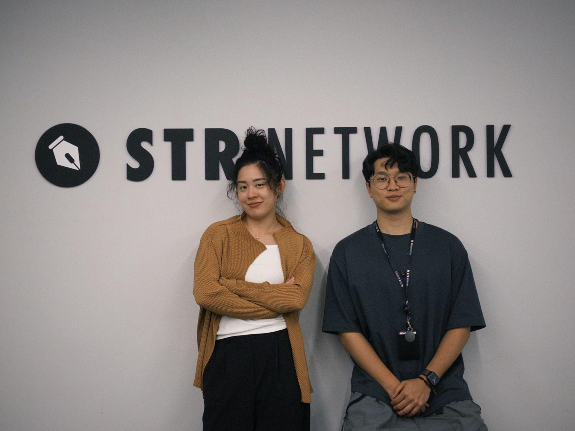 STR Network 共同創業者の Sunny とエンジニアの Feng、オフィスのロゴ前にて