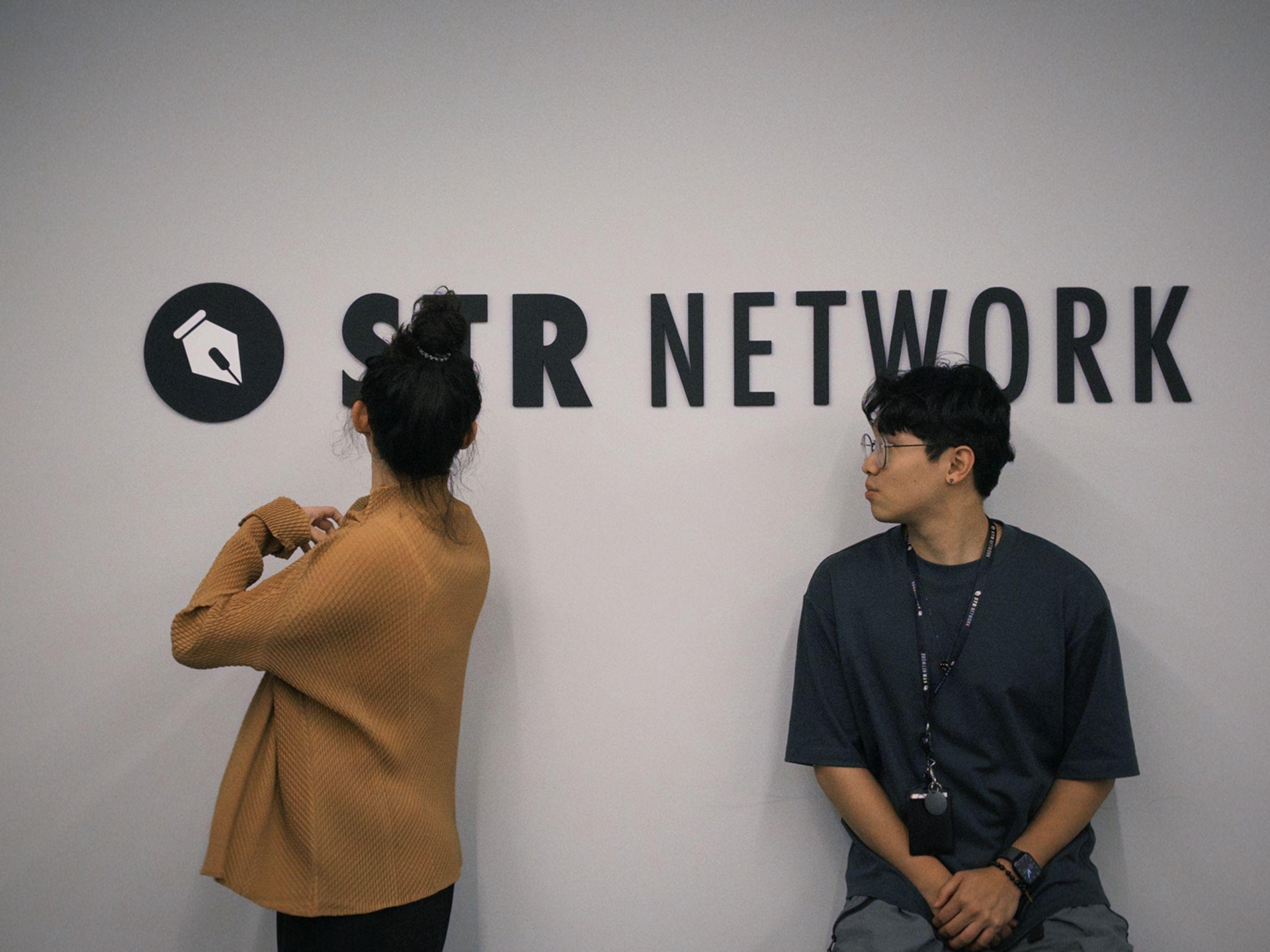 STR Network の Sunny と Feng、オフィスのロゴ前にて